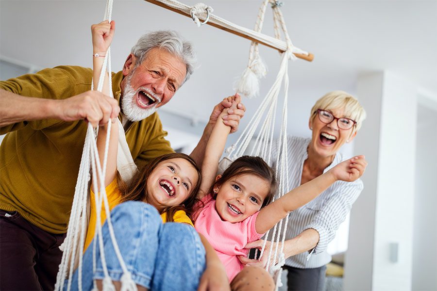 Contact - Cheerful Portrait of Grandparents Having Fun Swinging Their Grandchildren in an Indoor Hammock
